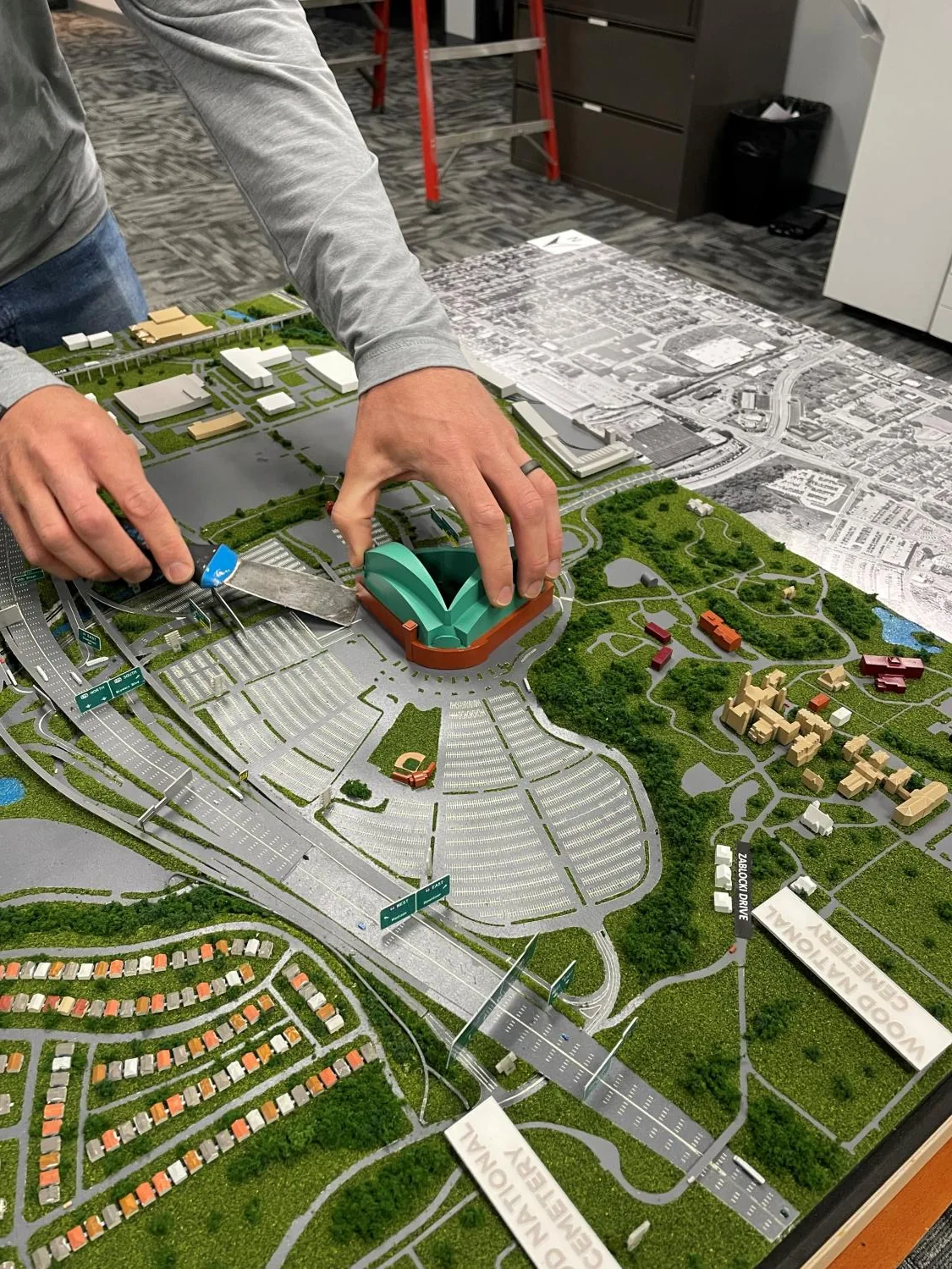 Hands carefully lifting the original simplified stadium from the I-94 model.